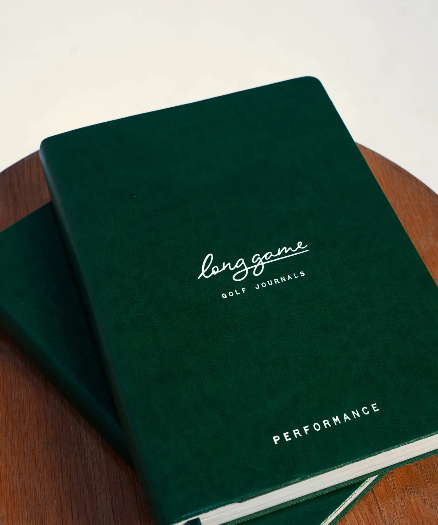 The Planner and the Performance Journal stacked together, green cloth covers with the Long Game mark